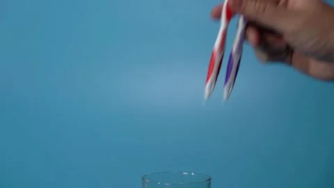 Hand Puts Two Plastic Multi-Colored Toothbrushes into a Glass Beaker Stock Footage 147850037