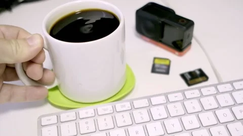 HAND PUTS WHITE CUP WITH COFFEE ON GREEN STAND NEXT TO COMPUTER KEYBOARD Stock Footage 150337491