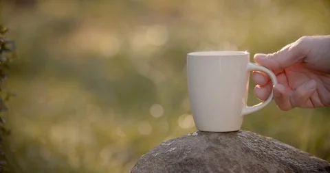 Hand puts a white steaming cup on the rock. Self-isolation in countryside. Video stock 128325045
