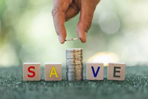 Hand putting coin on stack coin with word save on wooden cube in green boke.. Foto stock