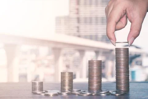 Hand putting coin on  stack growing graph with city background, The concept o Stock Photos