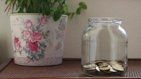 Hand putting coins into a jar one by one Stock Footage 133740757