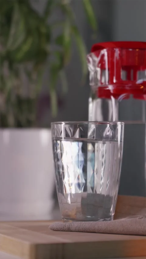 Hand putting down glass of pure water on table in warm morning light 스톡 동영상 344877104