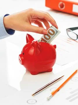 Hand putting hundred dollars note into piggy coins bank Stock Photos