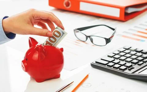 Hand putting hundred dollars note into piggy coins bank Stock Photos