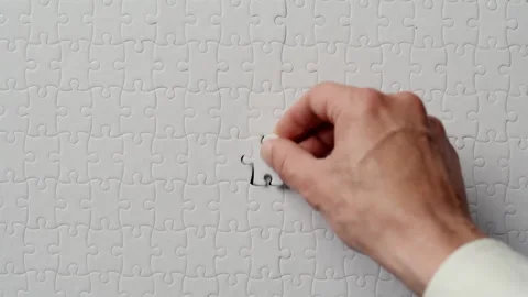 Hand putting last puzzle piece finishing closeup. White jigsaw being assembled Stock Footage 332309123
