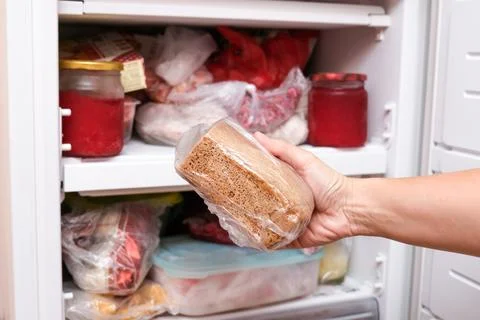 A hand putting loaf of brown bread in reserve on a shelf of a home freezer, long Stock Photos