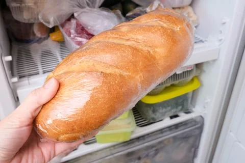 A hand putting a loaf of wheat bread in reserve on a shelf of a home freezer Stock Photos