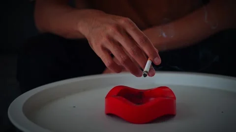 Hand putting out cigarette in red ashtray on white table Stock Footage 316887486
