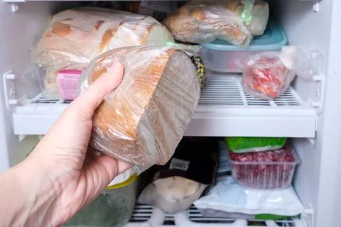 A hand putting a package of brown bread in reserve on a shelf of a home freezer Stock Photos
