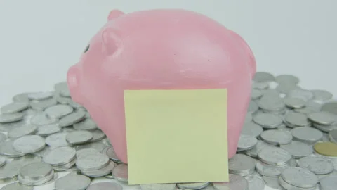 Hand Putting Yellow Note Paper Behind Pink Piggy Bank With Lot of Coins Stock Footage 293019692