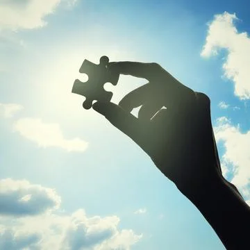 Hand, puzzle and solution with clouds in sky with problem solving, lens flare or Stock Photos