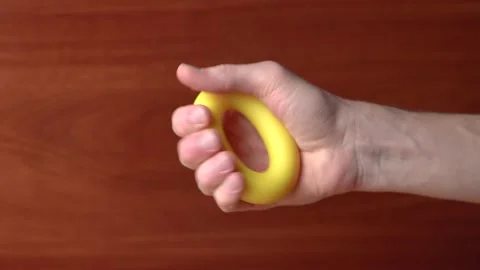 Hand quickly squeezes yellow hand expander many times against wooden background Stock Footage 145457691