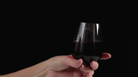 A hand raises a glass of wine, black background. Stock Footage