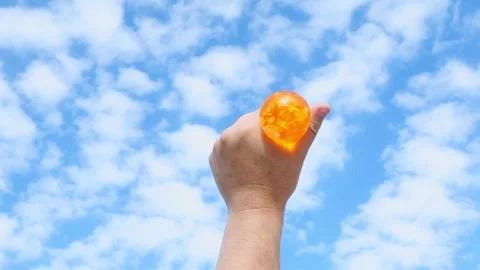 Hand raising orange translucent water balloon into blue sky Stock Footage 321241810