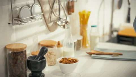 Hand reaches for almonds in a modern kitchen with organized jars and kitchen Stock Footage 323806250