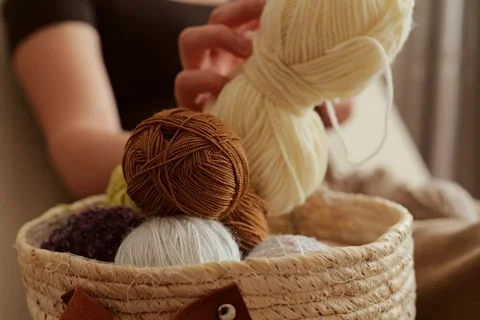A hand reaches into a basket filled with different colored yarn. The setting is Stock Footage 336464845