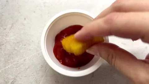 Hand reaches for a crispy chicken nugget and dips it into a bowl of red ketchup Stock Footage 336311450