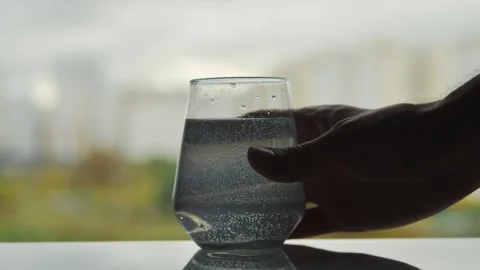 Hand reaches for glass with dissolving tablet, sparkling bubbles in water, soft Video stock 319029343