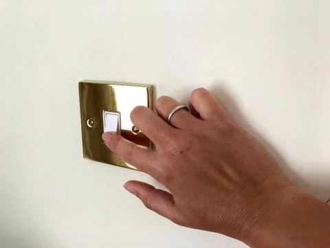 Hand reaches for light switch on white wall golden bezzel Stock Photos