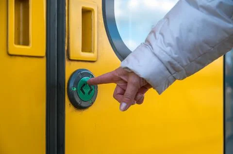 A hand reaches out to press a button on a yellow train door while waiting at  Stock Photos