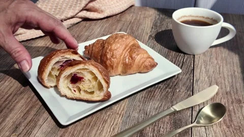 A hand reaches for a slice of pastry while a croissant sits nearby on a plate Stock Footage 336533316