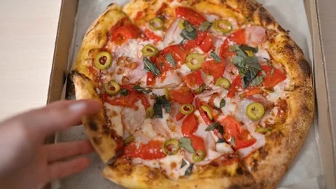 A hand reaches for a slice of pizza loaded with various toppings and flavors. Stock Footage 339005910