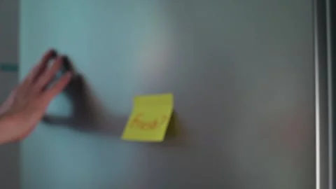 A hand reaches towards a sticky note on a fridge that reads Fresh? The setting Stock Footage 339096562