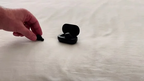 Hand Reaches for Wireless Earbud on Soft Fabric Surface Scene Stock Footage 325788892