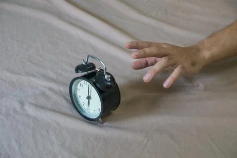 Hand reaching for the alarm clock on the bed. Stock Photos
