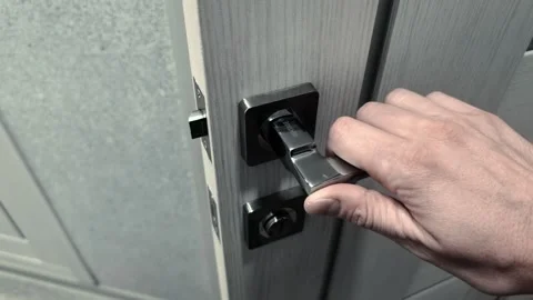 Hand reaching for and turning modern silver door handle on wooden door. Close up Stock Footage 339865225