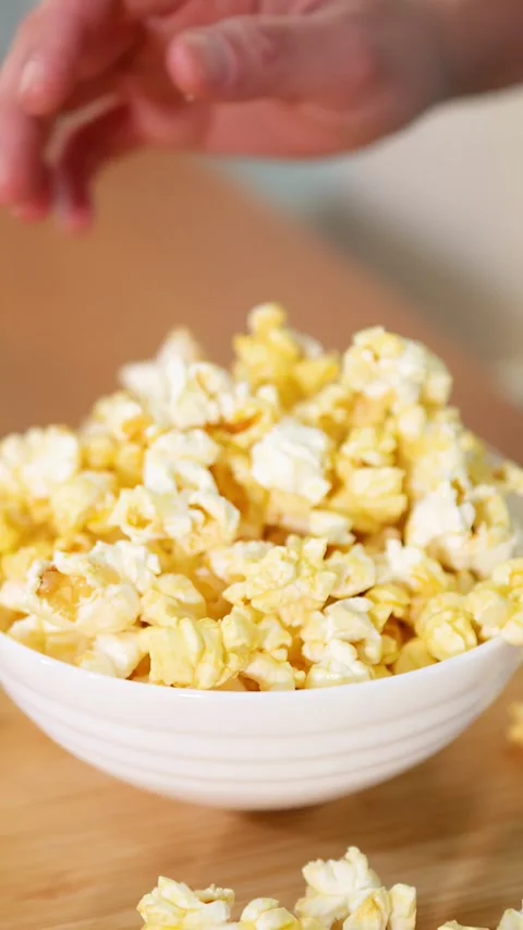 Hand Reaching for Buttery Popcorn in a White Bowl on Wooden Tray Stock Footage 335612610