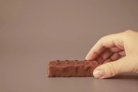 Hand reaching for a chocolate bar on a gray background Stock Photos