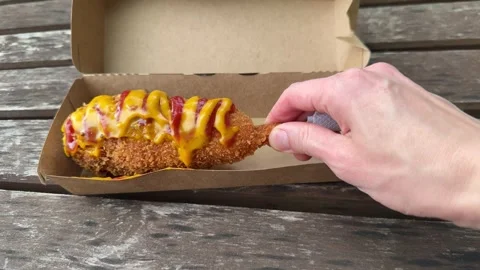 Hand reaching for corn dog with mustard and ketchup in cardboard box  Vídeos de archivo 338361654
