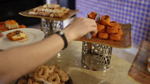 Hand reaching for crispy Middle Eastern sweets kunafa rolls golden layers pistac Stock Footage 310536394