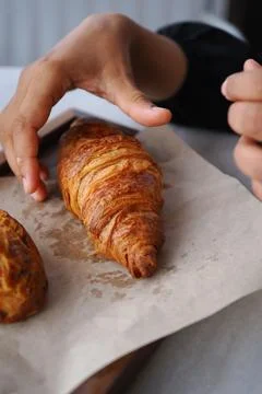 Hand reaching for a croissant in a cafe setting during morning hours Stock Photos