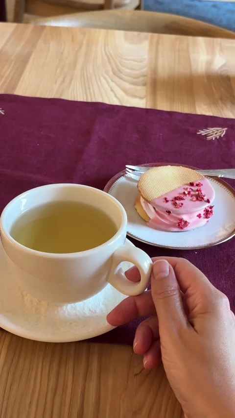 A hand reaching for a cup of tea served with a pink glazed cookie Stock Footage 338005591