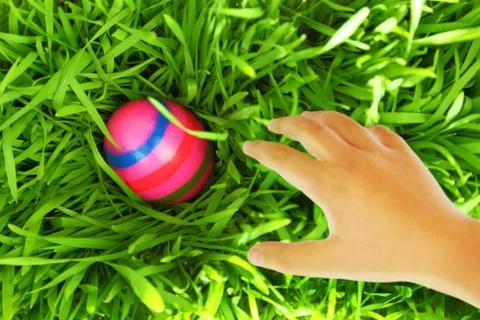 Hand reaching for Easter egg on green grass Stock Photos