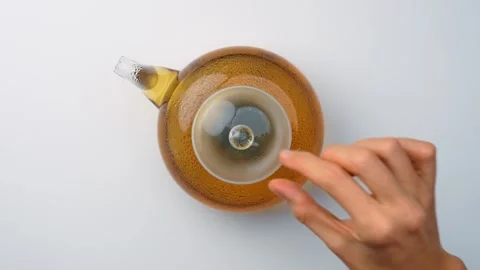 Hand reaching for glass teapot with brewed tea. Top view, female fingers near Stock Footage 342976544