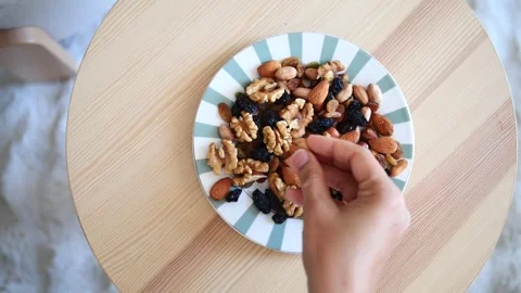 Hand reaching for mixed nuts on a wooden table Stock Footage 331274423