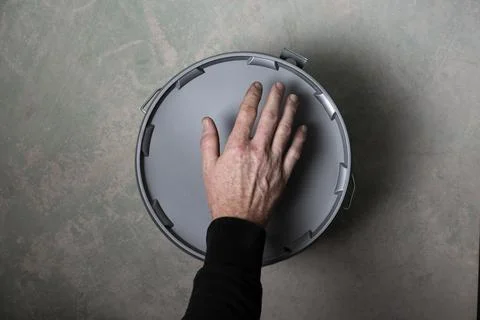 Hand reaching to open plaster bucket on concrete floor during home renovation Stock Photos