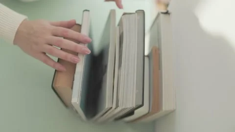 Hand reaching out to select a book from a stack, symbolizing curiosity Stock Footage 301240419