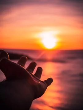 A hand reaching out to a setting sun with the light rays hitting the hand at  Stock Photos