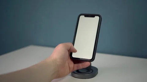 A hand is reaching out towards a smartphone that is positioned on a stand for Stock Footage 314465486