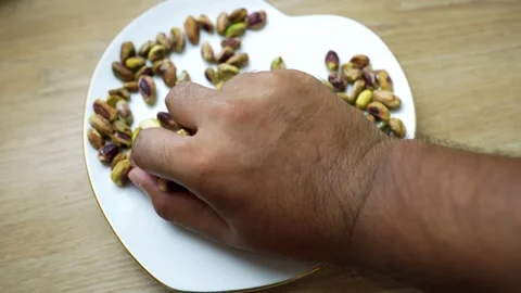 Hand reaching for pistachio nuts on a plate Stock Footage 320727432