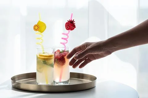 Hand reaching for refreshing summer lemonade and strawberry drinks Stock Photos