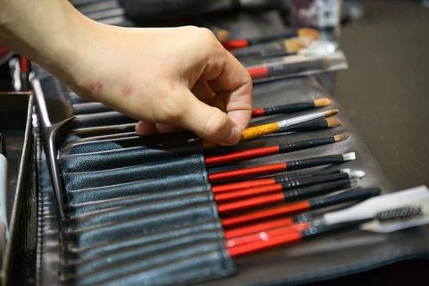 Hand reaching for row of make-up brush in leather brush roll. Stock Photos