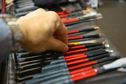 Hand reaching for row of make-up brush in leather brush roll. Stock Photos