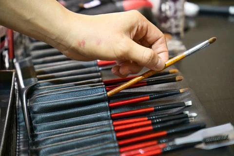 Hand reaching for row of make-up brush in leather brush roll. Stock Photos