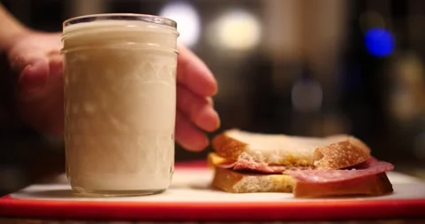 Hand reaching for sandwich taking a bit then drink a cup of milk in a glass Stock Footage 205257165